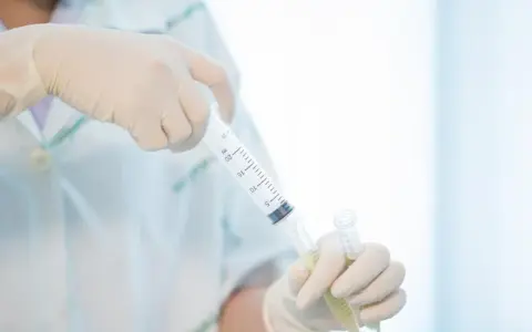 Ręce w rękawiczkach przygotowują pobranie płynu mózgowo rdzeniowego do analizy.