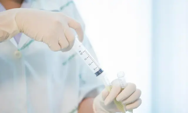 Ręce w rękawiczkach przygotowują pobranie płynu mózgowo rdzeniowego do analizy.